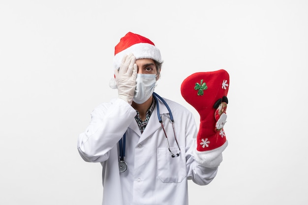Вид спереди мужчина-врач, держащий большой праздничный носок на белой стене, вирус covid holiday