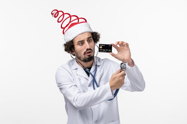 Front view of male doctor holding black bank card on the white wall