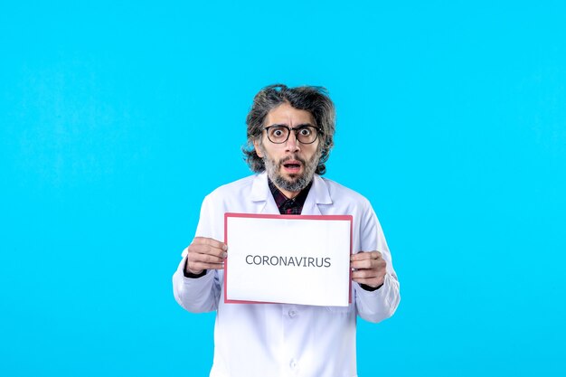 Front view male doctor holding coronavirus writing on blue