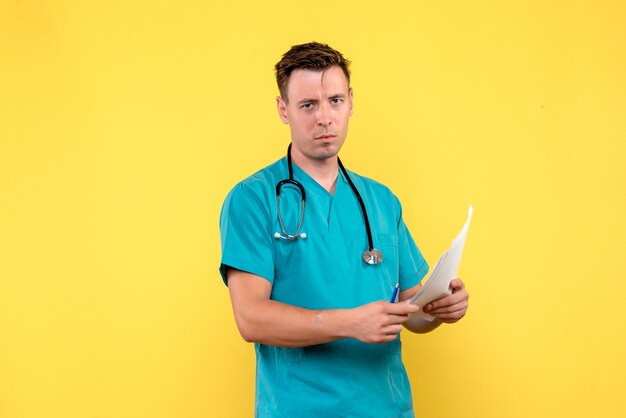 Front view of male doctor holding documents on a yellow wall