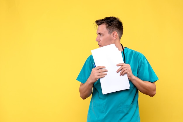 Front view of male doctor holding documents on a yellow wall