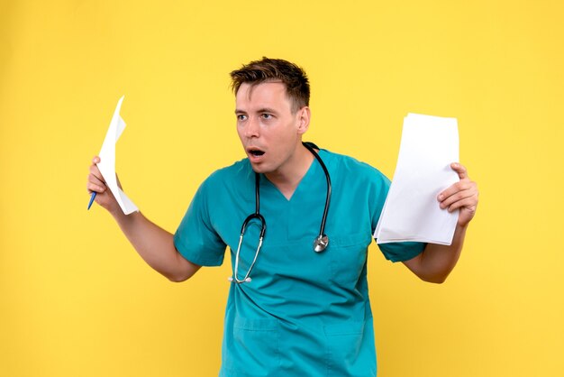 Front view of male doctor holding documents on the yellow wall