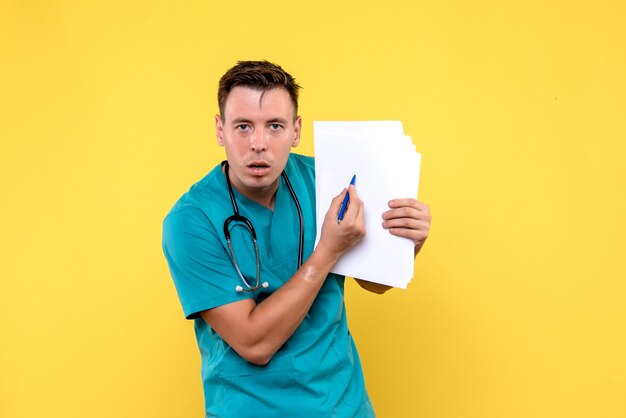Вид спереди мужчины-врача, держащего документы на желтой стене