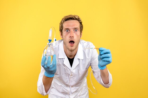 Front view male doctor holding dropper on yellow desk human pandemic medic covid-