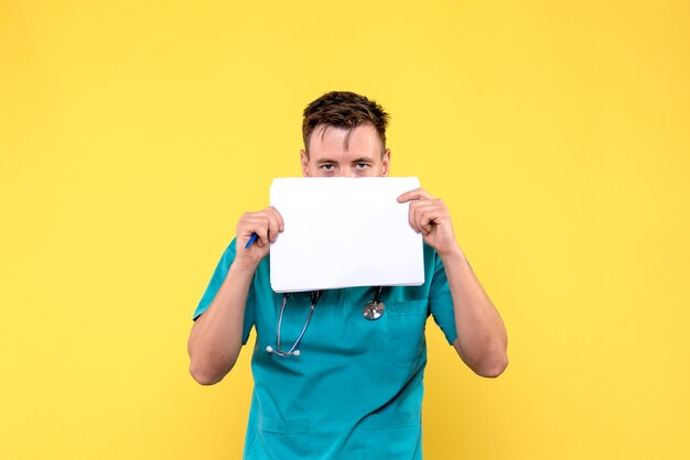 Front view of male doctor holding files on light yellow wall