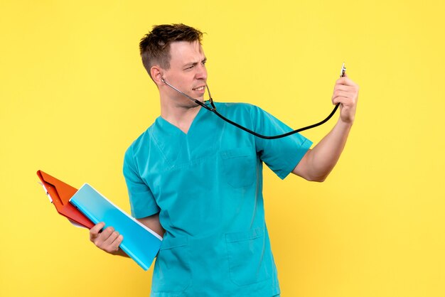Front view of male doctor holding files and tonometer on yellow wall