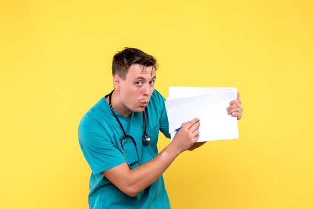 Front view of male doctor holding files on the yellow wall