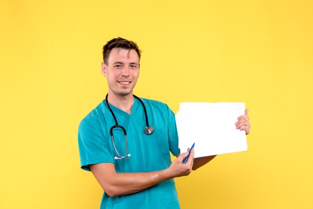 Front view of male doctor holding files on yellow wall