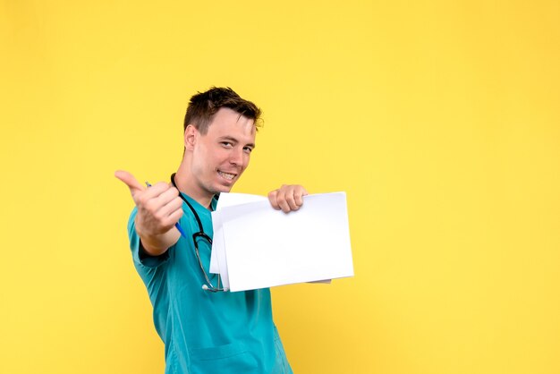 Front view of male doctor holding files on yellow wall