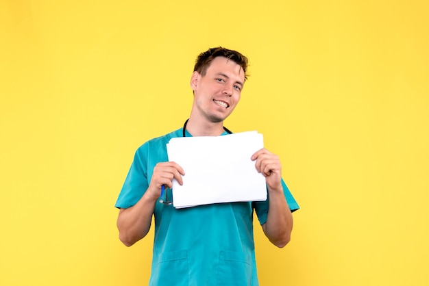 Front view of male doctor holding files on yellow wall