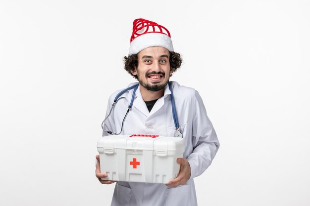 Front view of male doctor holding first aid kit on white wall