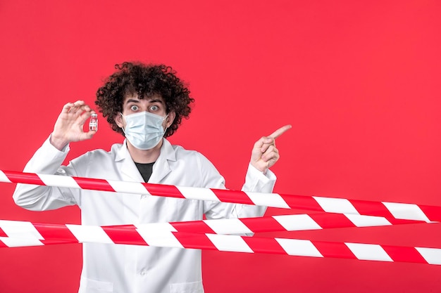 Front view male doctor holding flask with medicine on the red background covid- health danger uniform quarantine color medical warning