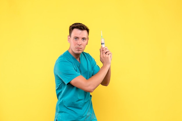 Front view of male doctor holding huge injection on yellow wall
