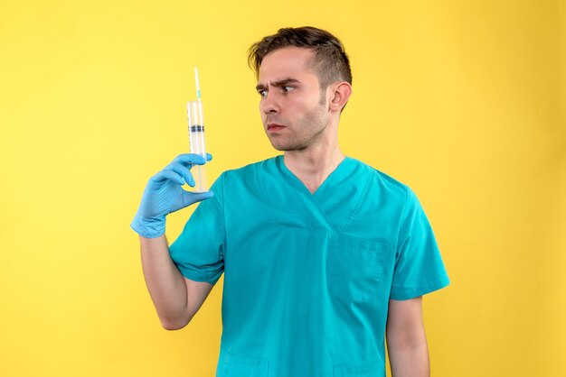 Front view of male doctor holding huge injection on yellow wall