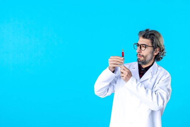 Front view male doctor holding injection on blue