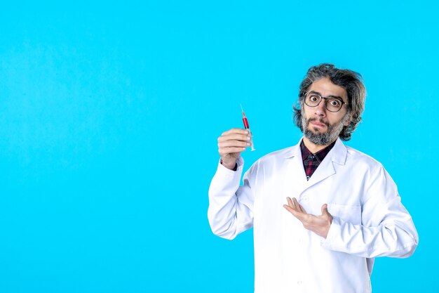 Front view male doctor holding injection on blue