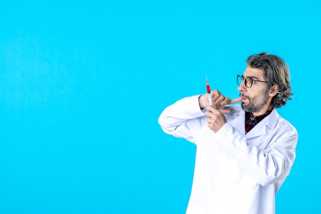 Front view male doctor holding injection on blue