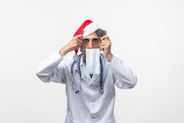 Front view male doctor holding mask on the white wall new year holiday virus covid