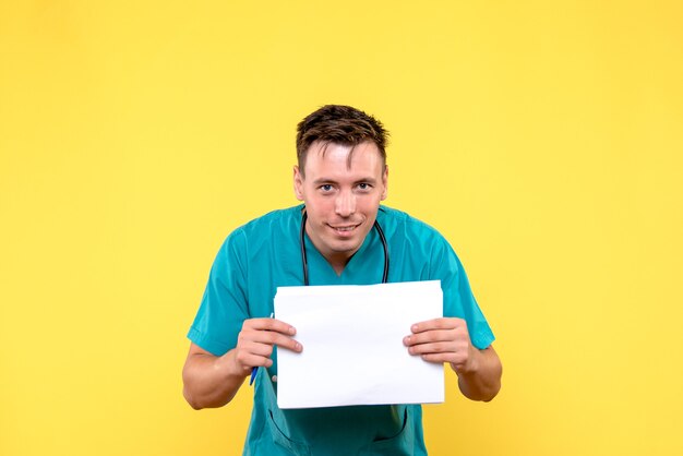 Front view of male doctor holding paper files on yellow wall