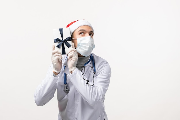 Front view of male doctor holding present on a white wall