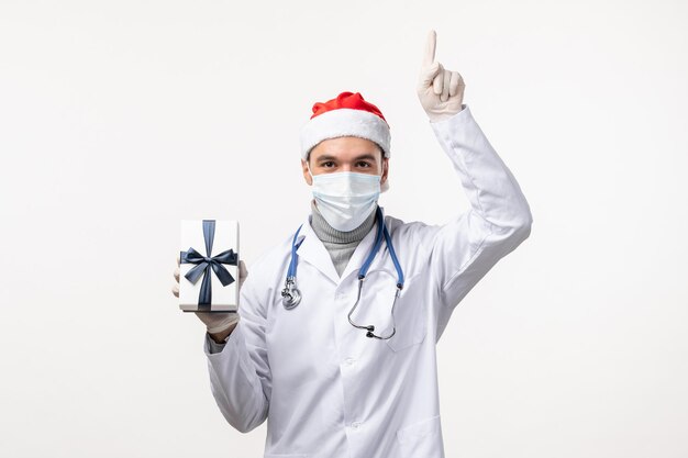 Front view of male doctor holding present on a white wall