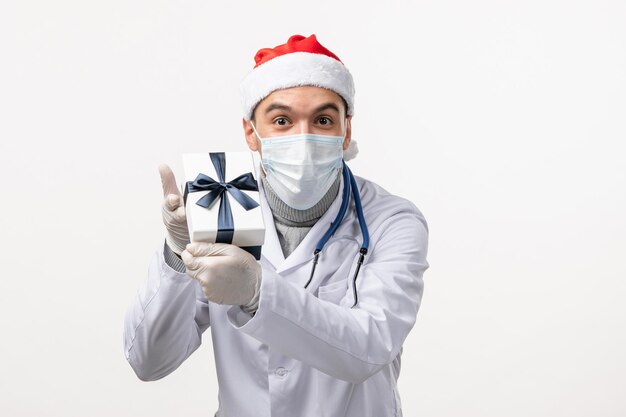 Front view of male doctor holding present on a white wall