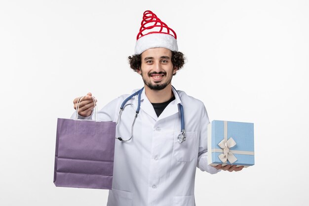 Вид спереди мужского врача, держащего подарки на белой стене
