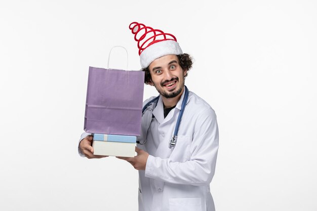 Front view of male doctor holding presents on white wall