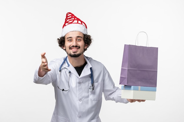 Front view of male doctor holding presents on white wall