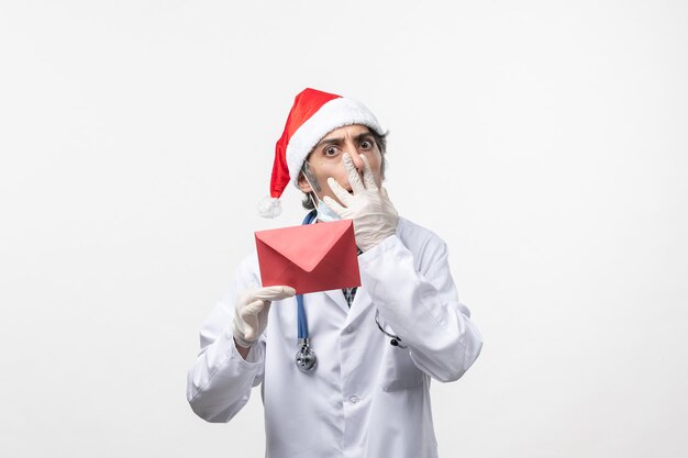 白い壁の健康covid-ウイルス病院に赤い封筒を保持している正面図男性医師