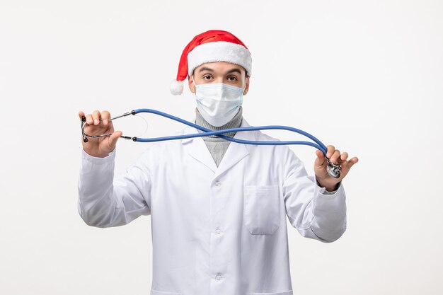 Front view of male doctor holding stethoscope on white wall