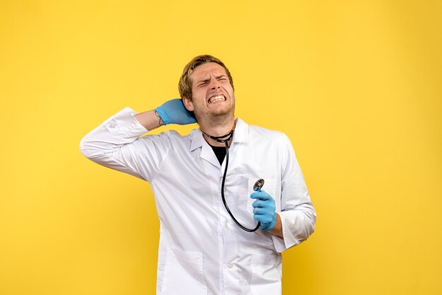 Front view male doctor holding stethoscope on a yellow background health human virus medic