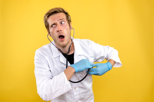 Front view male doctor holding stethoscope on yellow desk human health covid- medic
