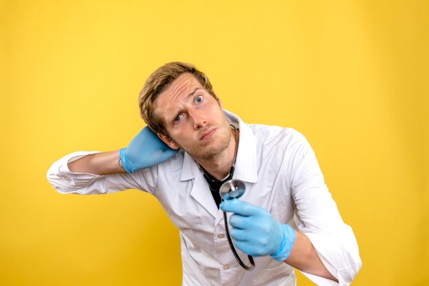 Вид спереди мужской доктор, держащий стетоскоп на желтом столе, здоровье человека, медик, covid-