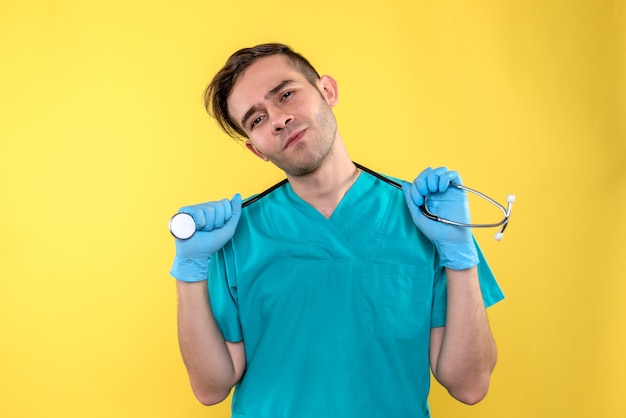 Front view of male doctor holding stethoscope on yellow wall