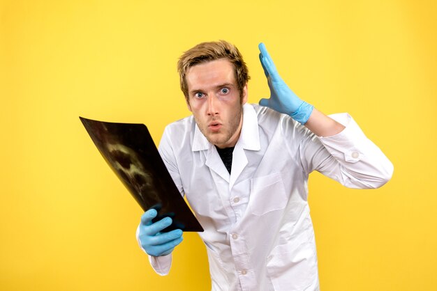 Front view male doctor holding x-ray on yellow background medic covid hygiene surgery