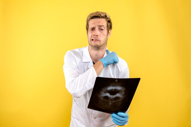 Вид спереди мужской врач, держащий рентген на желтом фоне, медик, хирургия, гигиена, covid