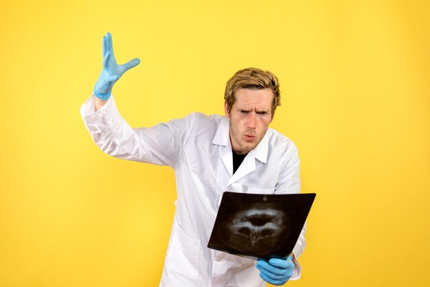 Free photo front view male doctor holding x-ray on yellow desk medic surgery hygiene covid-