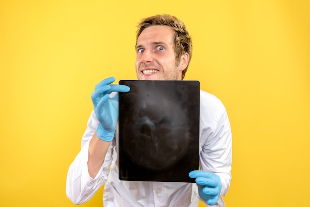Вид спереди мужской доктор, держащий рентгеновский снимок на желтом столе, медик, хирургия, гигиена, covid