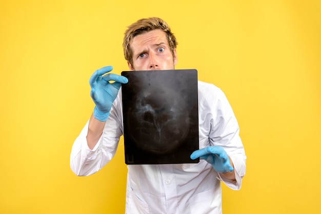 Free photo front view male doctor holding x-ray on yellow desk surgery medic covid hygiene