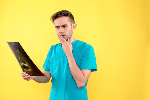 Front view of male doctor holding x-ray on yellow wall