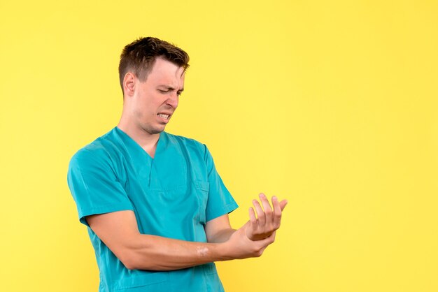 Front view of male doctor hurt his arm on yellow wall
