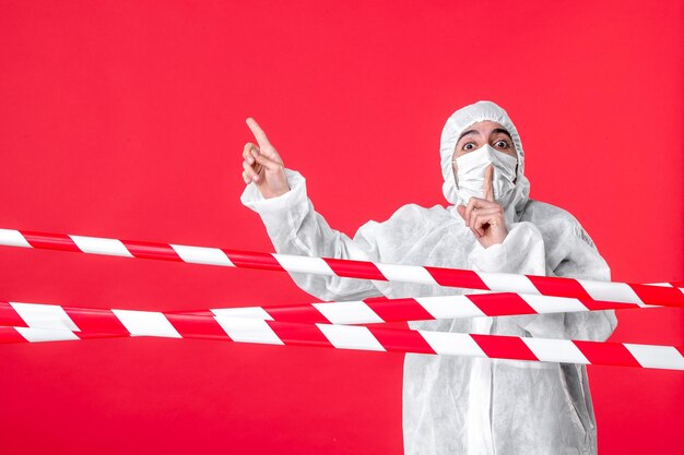 Бесплатное фото Вид спереди врач-мужчина в защитном костюме и маске на красном фоне лечебная больница covid-карантин цвет изоляции вируса