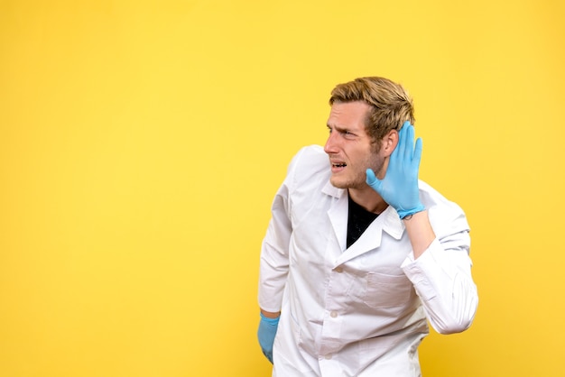 Вид спереди мужской доктор, слушающий на желтом фоне covid- пандемический медик здоровья
