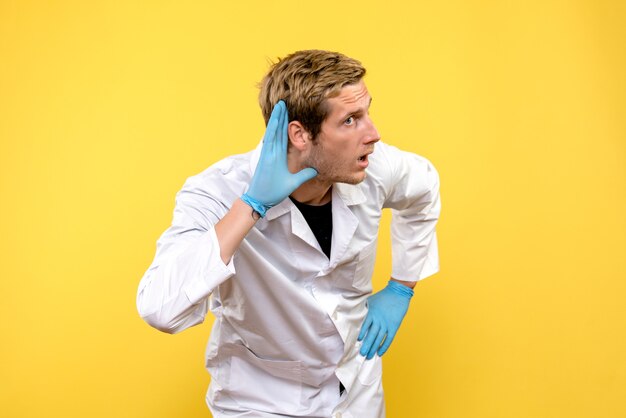 Front view male doctor listening on a yellow background health covid- pandemic medic