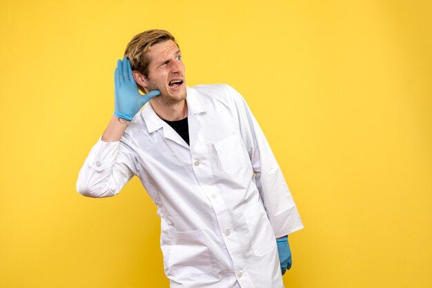 Front view male doctor listening on yellow background medic health covid pandemic