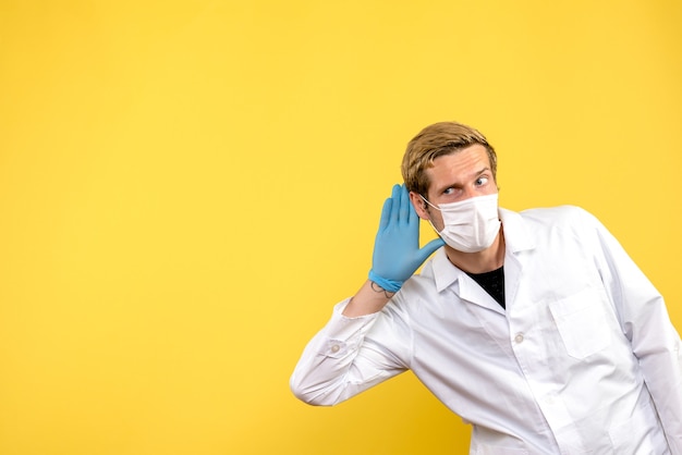 Front view male doctor listening on yellow background pandemic medic health covid- virus