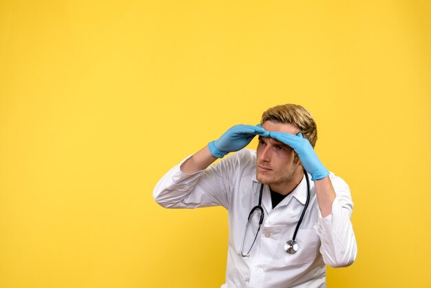 Front view male doctor looking at distance on yellow background health human virus medic