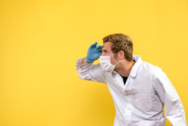 Front view male doctor looking at distance on yellow background health pandemic covid virus