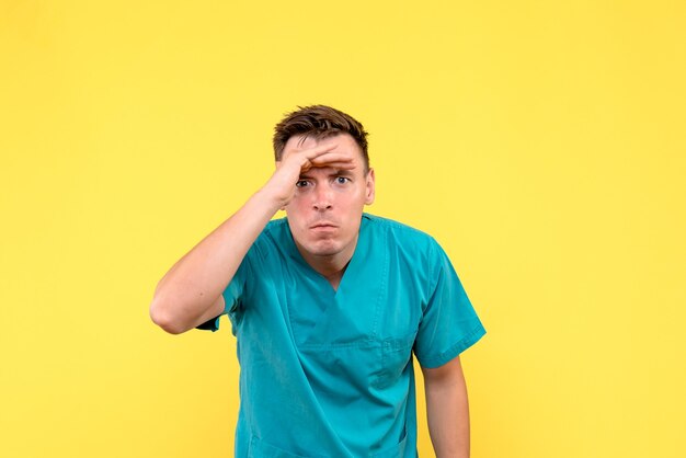 Front view of male doctor looking at distance on yellow wall